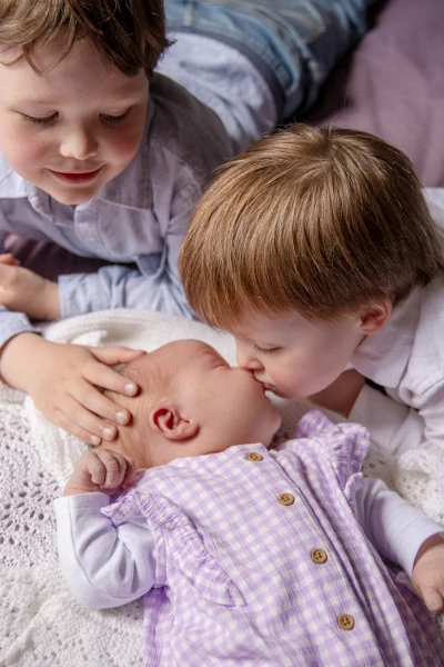 A child kissing his baby sister as his old brother cradles her head